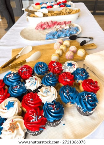 Wide view of a dessert table featuring red, white, and blue cupcakes alongside other colorful sweets. The setup is festive and brightly lit, suggesting a party or holiday event.