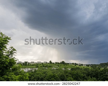 A wide view of a dramatic, dark shelf cloud rolling menacingly over a green residential valley community in Pennsylvania.