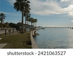 Wide view from Gulfport , Florida Marina looking west with s curve of concrete  seawall being repaired towards Boca Ciega Bay in afternoon sun. Green Palm trees on the side , calm water and blue sky.