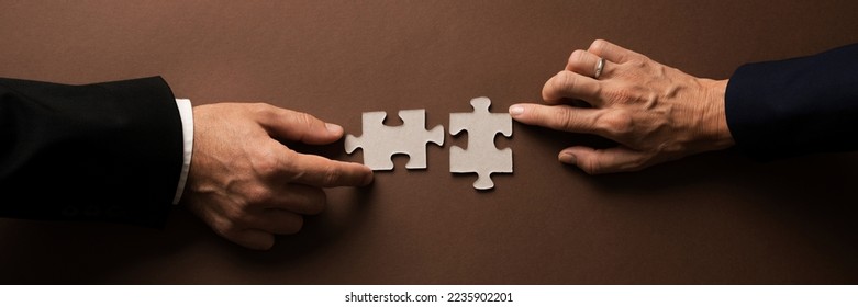 Wide view image of businessman and businesswoman hands joining two blank matching puzzle pieces. Over brown background. - Shutterstock ID 2235902201