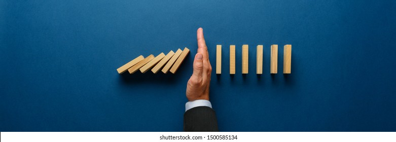 Wide View Image Of Businessman Hand Stopping Collapsing Dominos In A Conceptual Image. Top View Over Navy Blue Background.