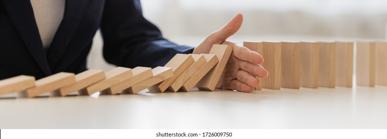 Wide view image of hand of businesswoman interrupting collapsing dominos in a conceptual image of preventing financial and market depression.