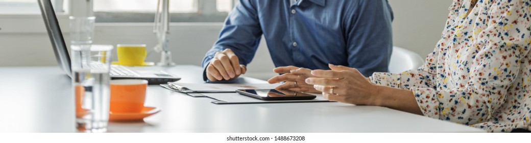 Wide View Image Of Male And Female Business Partners Working Together Sitting At Office Desk Reviewing Reports And Paperwork While Also
Using Digital Tablet.