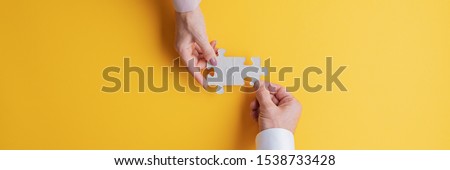 Wide view image of male and female hand joining two matching puzzle pieces together in a conceptual image of teamwork and cooperation. Top view with copy space.