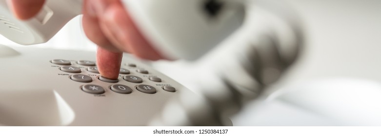 Wide View Image Of Male Hand Holding White Telephone Handset Dialing A Phone Number. Closeup View.