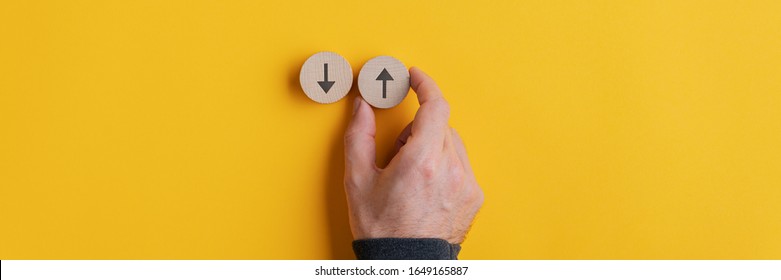 Wide View Image Of Male Hand Placing Two Wooden Cut Circles With Arrows Pointing Up And Down Over Yellow Background. 