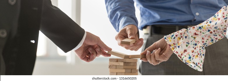 Wide View Image Of Three Businesspeople Building A Tower Of Wooden Pegs In A Conceptual Image Of Business Start Up And Teamwork.