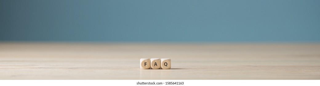 Wide view image of three wooden cubes spelling faq placed on wooden desk. Over blue background with plenty of copy space.