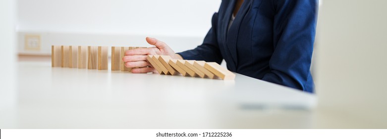 Wide View Image Of Unrecognizable Business Woman Sitting At Her White Office Desk Stopping Collapsing Dominos With Her Hand In A Conceptual Image Of Crisis Management.