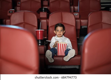 Wide View Of A Little Kid Eating Popcorn And Enjoying A Movie While Sitting In An Empty Cinema Theater