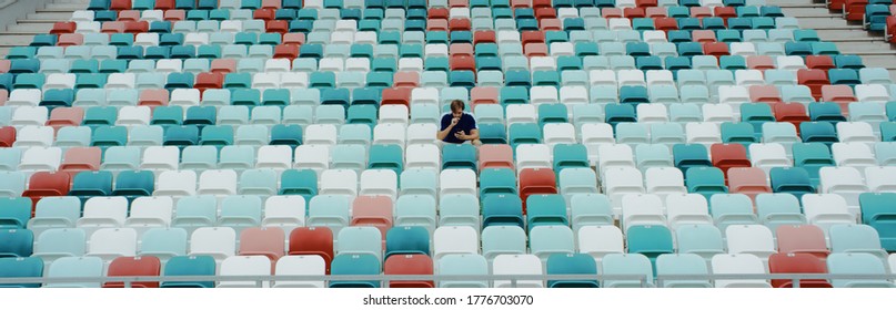 WIDE View Of A Lonely Fan Spectator Attending A Sports Event On An Empty Stadium. Isolation, Events During Coronavirus Pandemic Concept