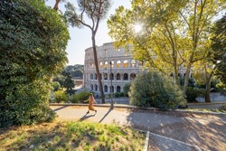 Wide View On Coliseum From Park Near By, Small Female Figure Running On Path. Landscape Of The Most Famous Landmark In Rome