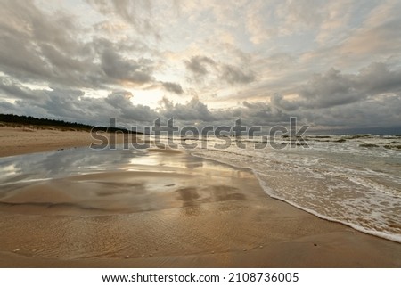 Wide view over a deserted stretch of beach, in the foreground shallow water with view leading to the horizon, above partly dramatic clouds announcing a change of weather, Slowinski Park Narodowy