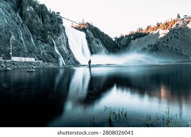 Wide view of a powerful waterfall cascading down rocky cliffs with mist rising over a reflective pool