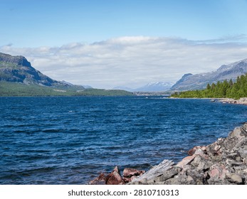 Wide view of the river flowing through Stora Sjöfallet National Park, surrounded by rugged mountains and boreal forest in Swedish Lapland. Scenic summer landscape in the UNESCO World Heritage area of Laponia.