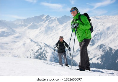 A Wide View Of A Senior Couple Hiking On The Slopes Of A Snowy Mountain With Man Smiling And Looking Up Into The Sky