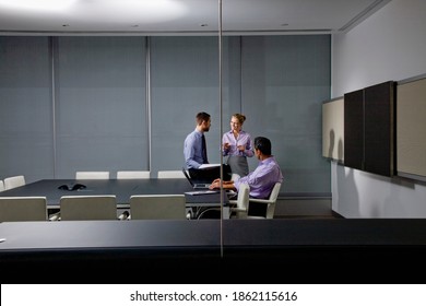 A wide view of a small group of business people talking with each other in the conference room while working on a project till late in the night