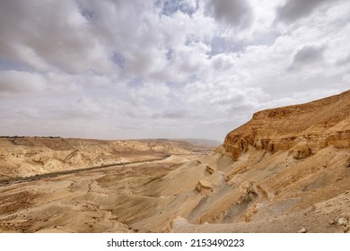 Wide View Of Steep Desert Mountains And Edged Cliffs, Vast Canyon Of And Winding River (Nahal Zin) With Fertile Vegetation. Hot Summer Morning In Midreshet Ben-Gurion, Negev, Israel