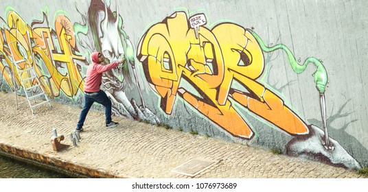 Wide View Of Street Artist Painting Colorful Graffiti On Generic Wall - Modern Art Concept With Urban Guy Performing And Preparing Live Murale With Multi Color Aerosol Spray - Retro Vintage Filter