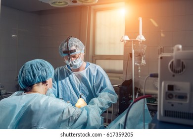 Wide view of a team of four surgeons operating on a patient in a dark OR at a hospital