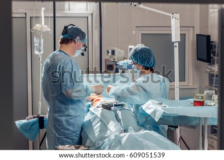 Wide view of a team of four surgeons operating on a patient in a dark OR at a hospital
