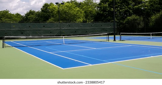 Wide view of two blue and green tennis courts that are also lined for pickleball games. - Powered by Shutterstock