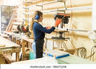 Wide view of a young woman working as a carpenter and using a drill press for her woodwork - Powered by Shutterstock