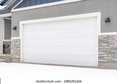 Wide White Garage Door Of Home With Gray Exterior Wall On A Snowy Winter Day