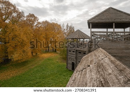 A wide-angle, elevated view from the fortress structure shows the tall log-built guard tower on the right, balanced by a dense grove of bright yellow and orange autumn trees 