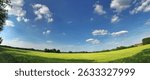 Wide-angle image displaying a verdant meadow with a stunning blue sky and fluffy clouds. The landscape embodies tranquility and the beauty of nature, perfect for headers and landscape emphasis.