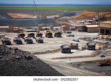 Wide-angle overview of modern Australian gold mine. Massive yellow excavation trucks line up for lunch. Used for transporting mine ore. Industrial transportation. All logos removed.