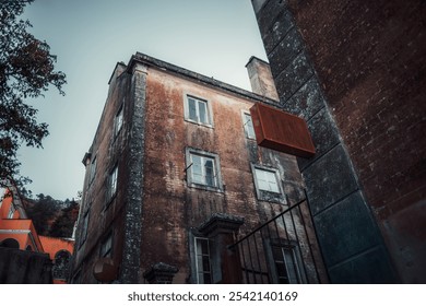 A wide-angle shot of an aged, weathered brick building with a faded facade and framed windows. Rusted mock-up sign protrudes from the wall, adding a vintage, abandoned feel - Powered by Shutterstock