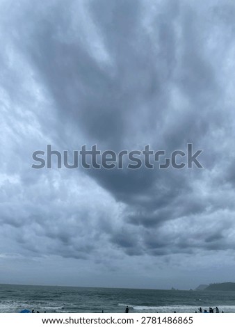 A wide-angle shot capturing dark, rolling storm clouds hovering over the wavy green waters of Haeundae Beach in Busan.