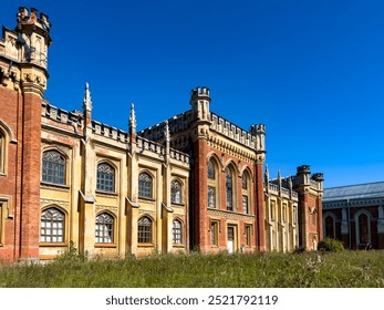 A wide-angle shot of a grand historic estate with intricate Gothic architecture, featuring tall arched windows and decorative towers. The scene is set on a sunny day with a vibrant blue sky - Powered by Shutterstock