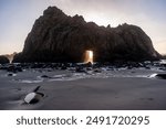 Wide-angle shot of the keyhole arch at Pfeiffer beach, California, whit the setting sun peeping through the central hole. Sunset on a winter evening in California.