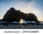 Wide-angle shot of the keyhole arch at Pfeiffer beach, California, whit the setting sun peeping through the central hole. Sunset on a winter evening in California.