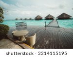 A wide-angle shot with a selective focus on the wicker table of a street bar of a luxurious Maldives resort in the foreground; a group of typical hotel bungalows with triangle roofs in the background