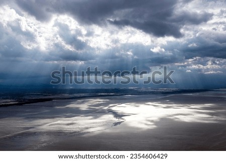 A wide-angle shot of the sun shining through clouds onto the land and sea beach. represents the power of nature. The sun is the power of life. The light from the sun nourishes all living things.