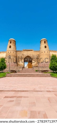 Wide-angle vertical view of the historic mud-brick twin towers and stone gate of the ancient Hisor Fortress under a clear bright blue sky