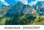 Wide-angle view of the Bockmattli limestone range and alpine meadows in the Schwyz canton of Switzerland with dramatic rock formations, forests and open summer sky

