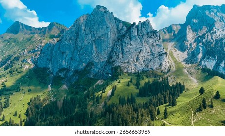 Wide-angle view of the Bockmattli limestone range and alpine meadows in the Schwyz canton of Switzerland with dramatic rock formations, forests and open summer sky


