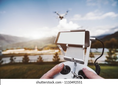Wide-angle view of the done remote controller in male hands with the smartphone blank screen template above, UAV is flying in the distance ready to film mountains and hills in a defocused background