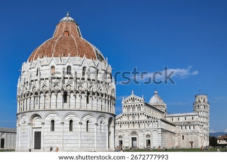 A wide-angle view of the iconic Piazza dei Miracoli (Square of Miracles) in Pisa, Italy, showcasing the historic Baptistery of St. John, the Duomo, and the world-famous Leaning Tower. The clear blue s