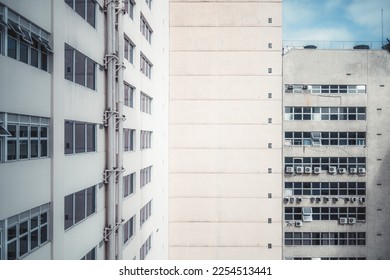 A wide-angle view of an inner corner of two buildings with plenty of windows, outdoor air conditioning units on a plastered facade, and pipes on a sunny day; the elevation of a house from a high floor