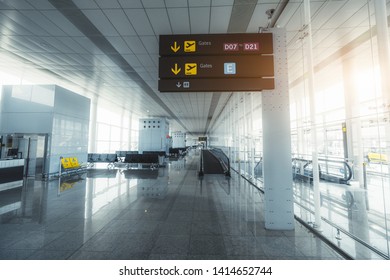 Wide-angle view of a long empty hall of a modern airport terminal with a bright glass facade on the right, the signpost with arrows and information, the travelator, gates, and rows of plastic seats