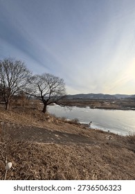 A wide-angle view of a long infrastructure bridge spanning over a partially frozen river during a clear blue sunset.