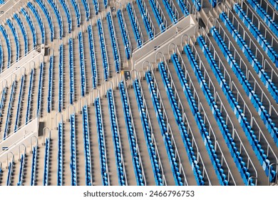 Wide-angle view of numerous rows of empty blue stadium seats. Seats are uniformly arranged, creating symmetrical and organized pattern. 