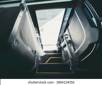A wide-angle view with selective focus from inside of a regular intercity bus entrance with opened door and with steps with yellow borders, a door to the toilet on the left, chromed railings
