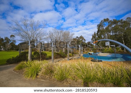 Wide-angle view showing timber arbor structures, native grass garden beds, basketball half-court area, and open green space under a partly cloudy sky at Bullion Park in Aintree.