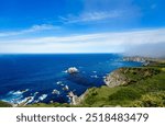 Wide-angle view of a stunning Pacific Ocean beach near Highway 101 in the San Francisco Bay Area, featuring vibrant rock formations, lush green grass, and a brilliantly blue ocean.